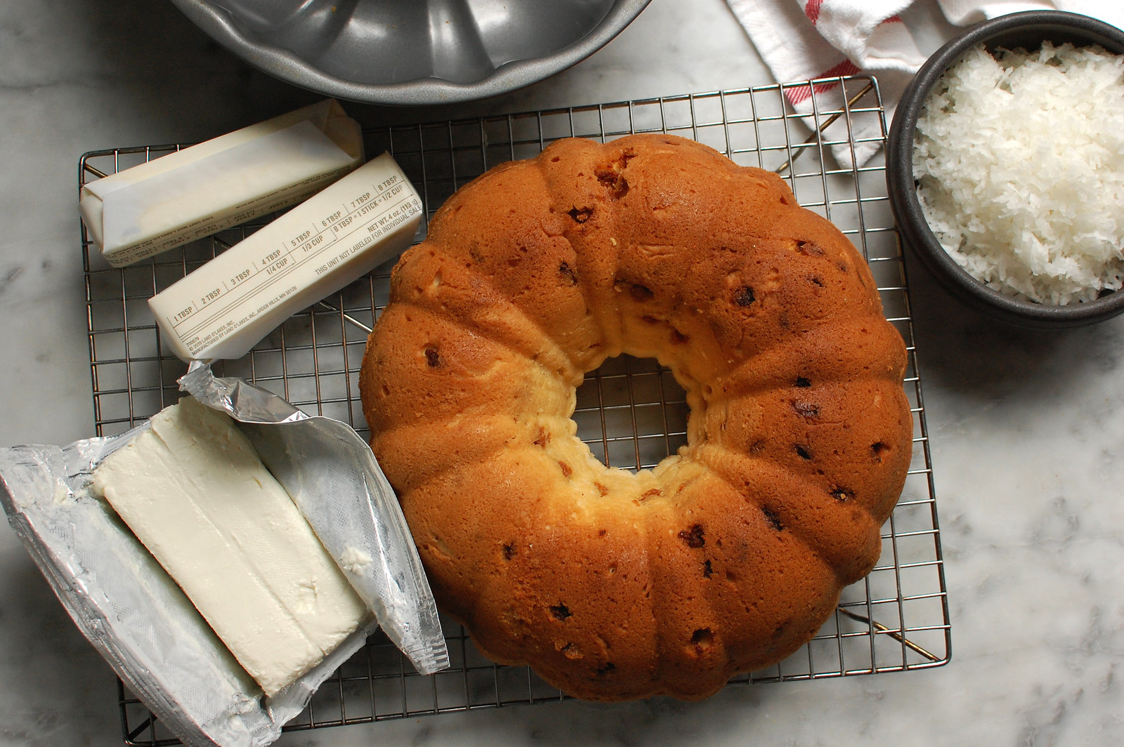 Tom Cruise Coconut Cake - Copycat Doan's Recipe Baked bundt cake on cooling rack next to frosting ingredients.