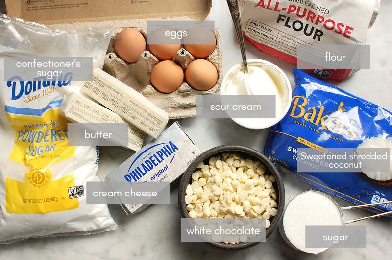 ingredients for copycat tom cruise coconut cake on kitchen counter, including: eggs, butter, white chocolate chips, coconut, flour, sugar, and confectioners' sugar.