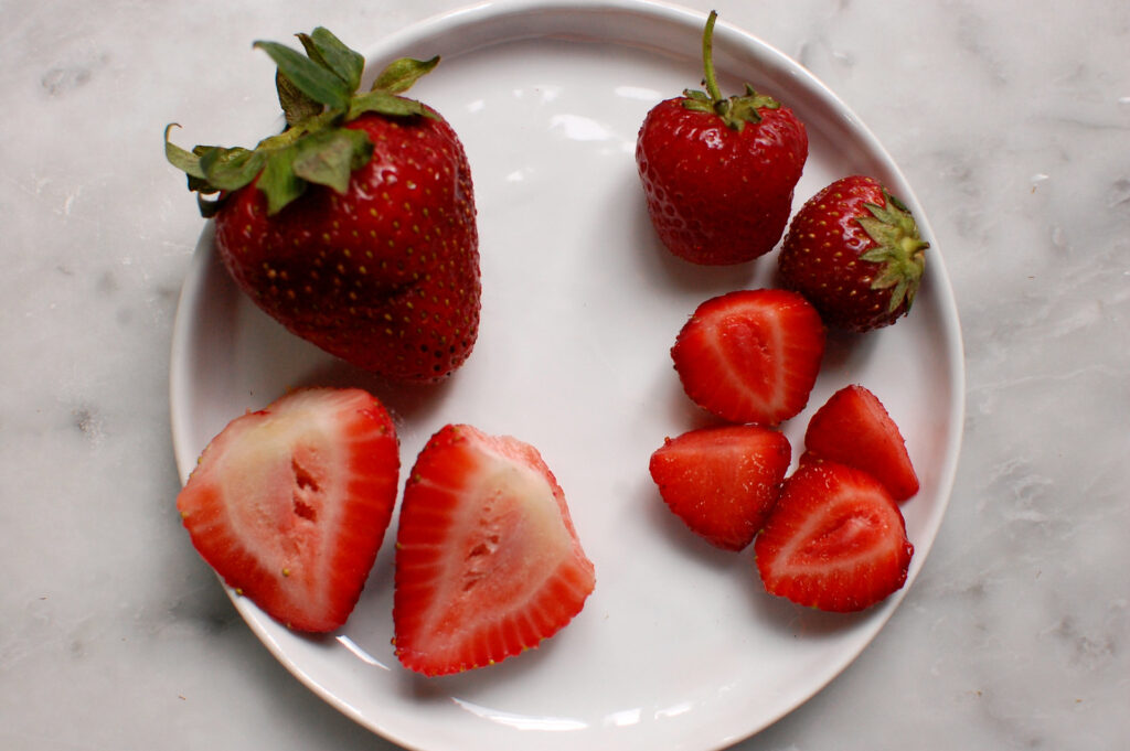 side-by-side view of large, white-interior, low-quality strawberries and small, concentrated red sweet strawberries to show which strawberries to choose for best results