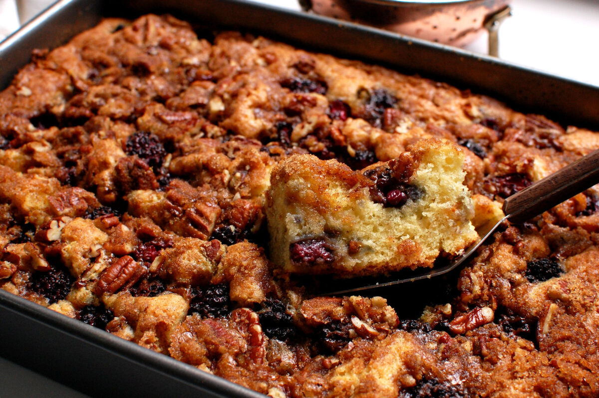 big square of moist blackberry coffee cake being removed from baking pan