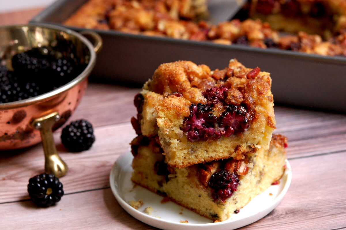stack of blackberry coffee cake pieces with coffee cake in baking pan in background