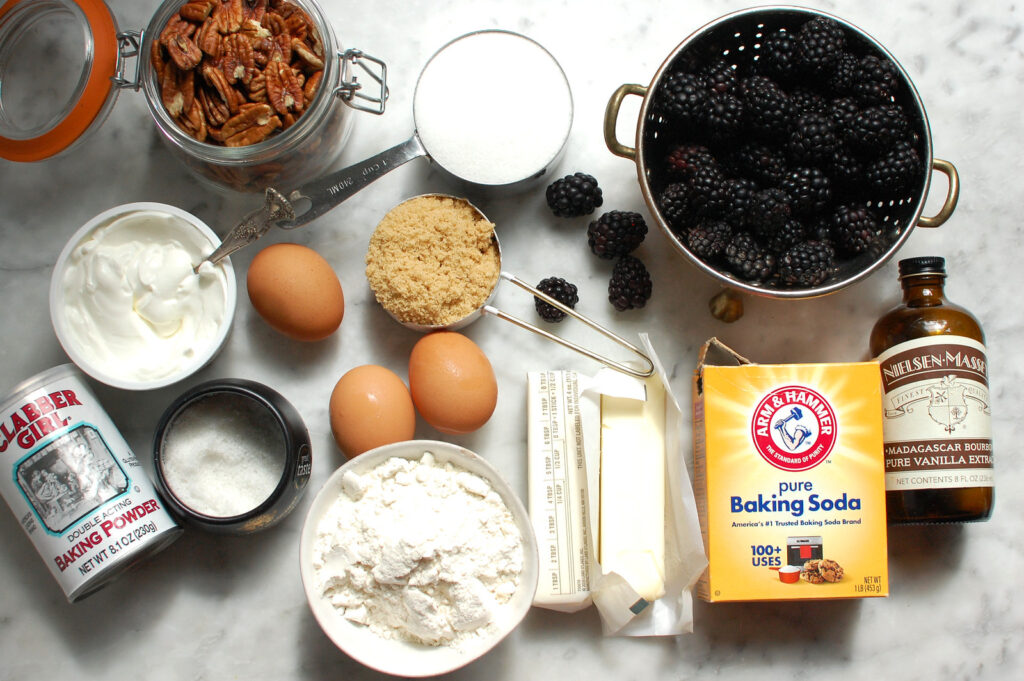ingredients for blackberry coffee cake, including flour, sugar, brown sugar, nuts, cinnamon, eggs, sour cream, and blackberries