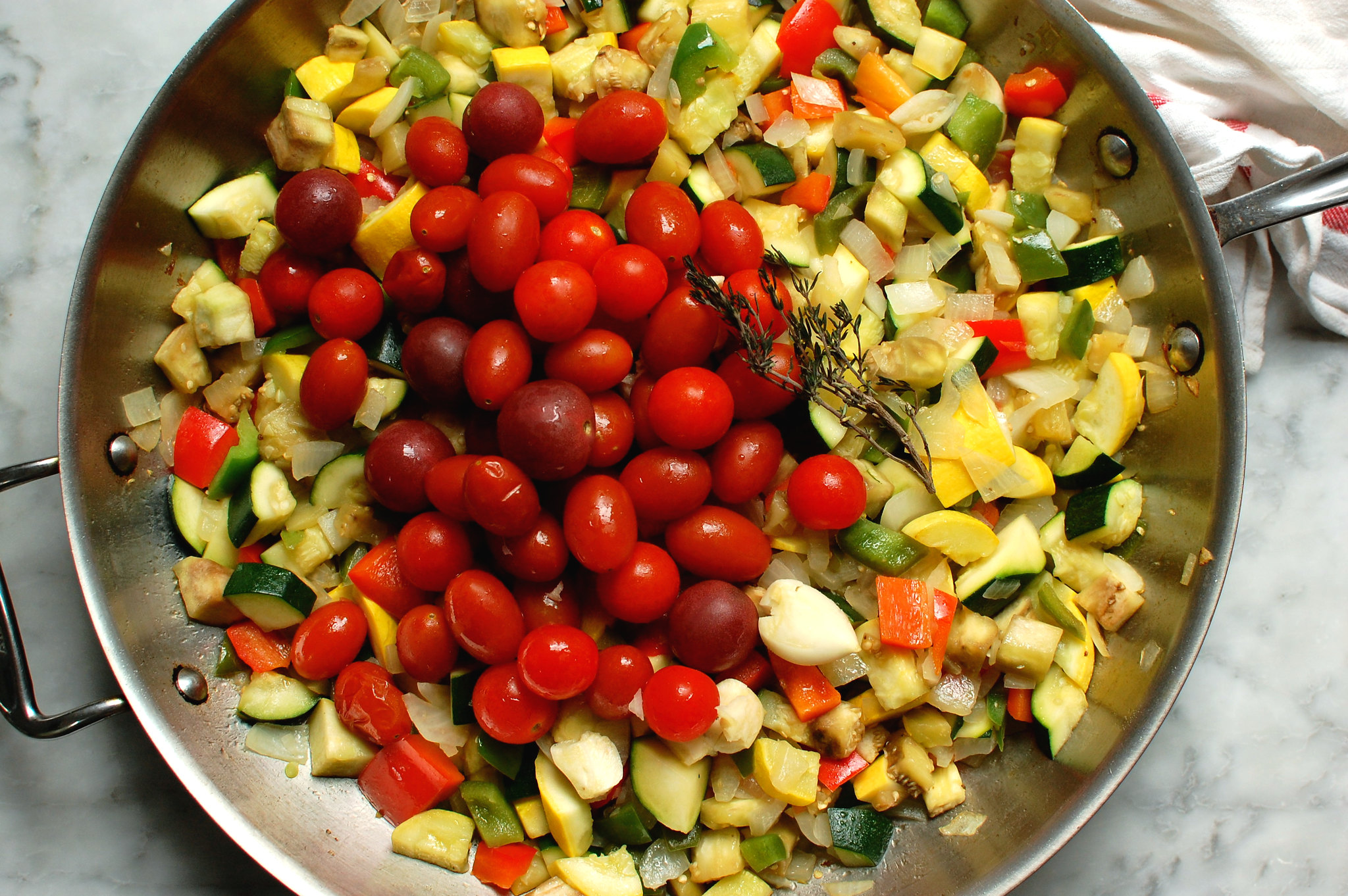 skillet with summer vegetables like tomato, eggplant, and squash being cooked into ratatouille