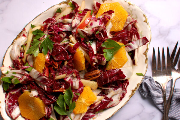 radicchio salad with citrus, apple slices, herbs, cheese, and toasted pecans on serving platter.