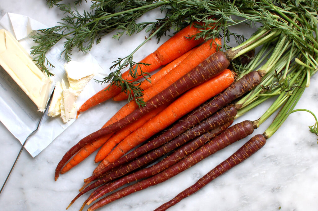 bunch of fresh carrots with green tops on marble countertop before roasting