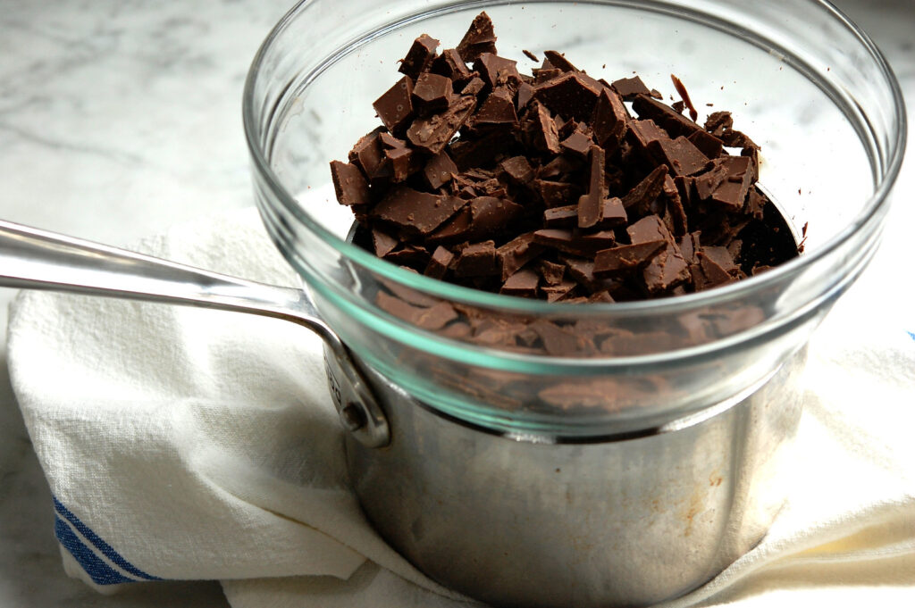 Chopped dark chocolate in mixing bowl over pot to melt in double boiler