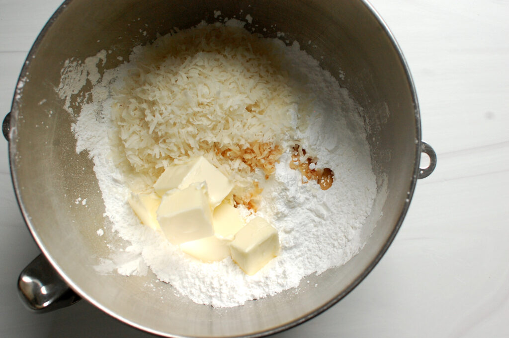 coconut cream dough ingredients powdered sugar, vanilla, coconut, and butter in mixing bowl before mixing