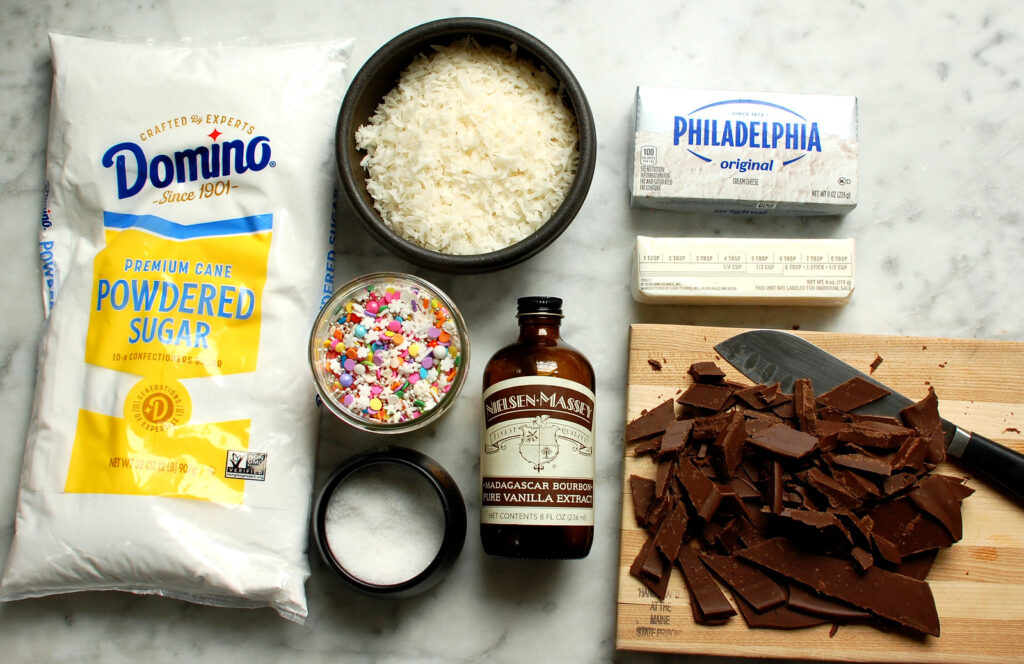 Ingredients for coconut cream Easter eggs, including: sweetened coconut flakes, powdered sugar, cream cheese, butter, vanilla, and dark melting chocolate.