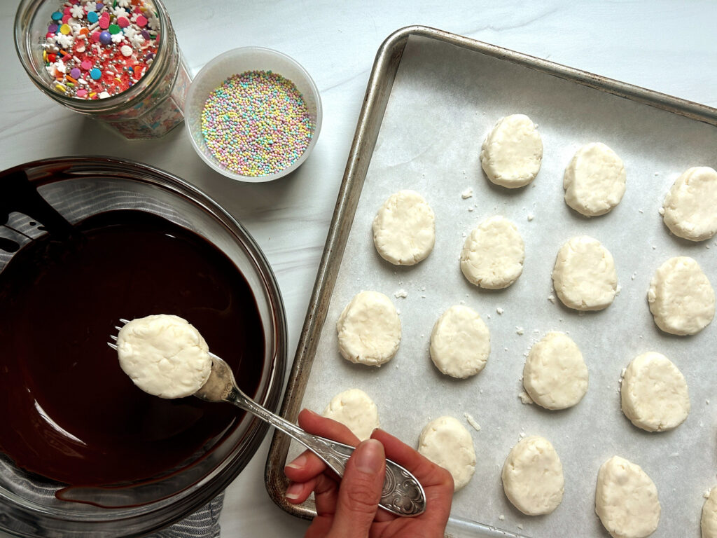Dipping coconut cream eggs in melted chocolate coating by hand with a fork.
