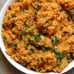 Flavorful quinoa cooked in broth with onion and tomato paste in a bowl garnished with parsley.