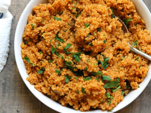 Flavorful quinoa cooked in broth with onion and tomato paste in a bowl garnished with parsley.