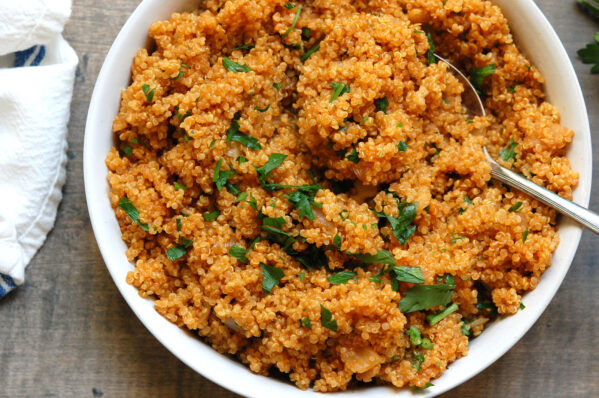 Flavorful quinoa cooked in broth with onion and tomato paste in a bowl garnished with parsley.